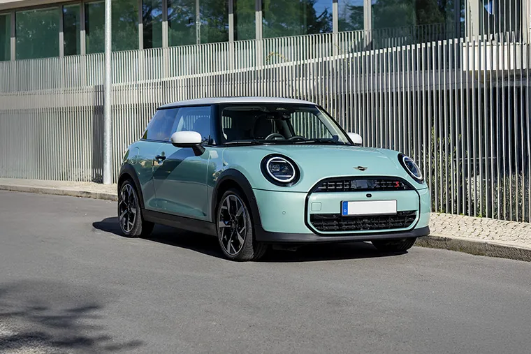 Mint green MINI Electric Hatch parked in front of a modern building under blue sky