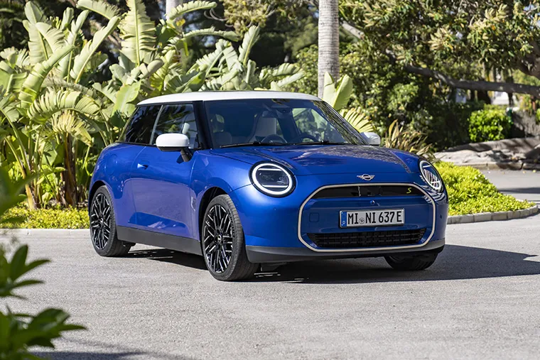 Blue MINI Cooper Electric parked in a sunny tropical setting.