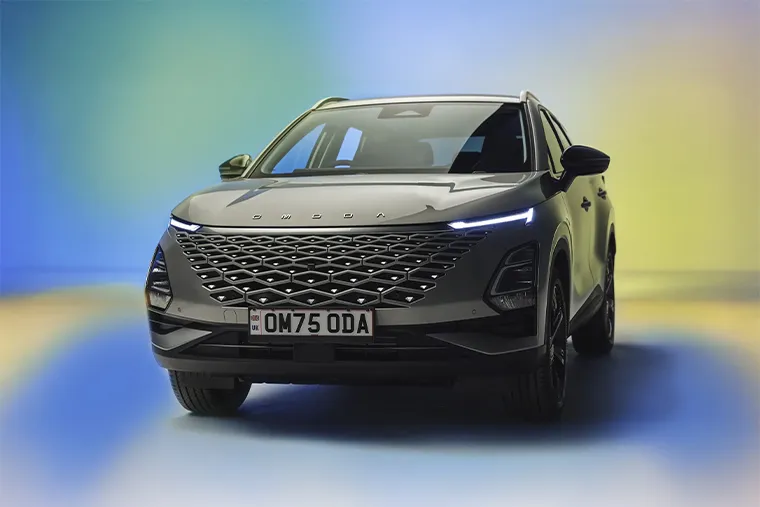 Front view of a silver SUV with futuristic LED headlights and a large diamond-pattern grille under studio lighting.