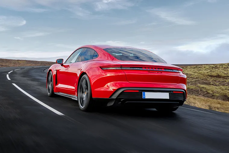 Rear view of a red Porsche Taycan driving on a winding open road.
