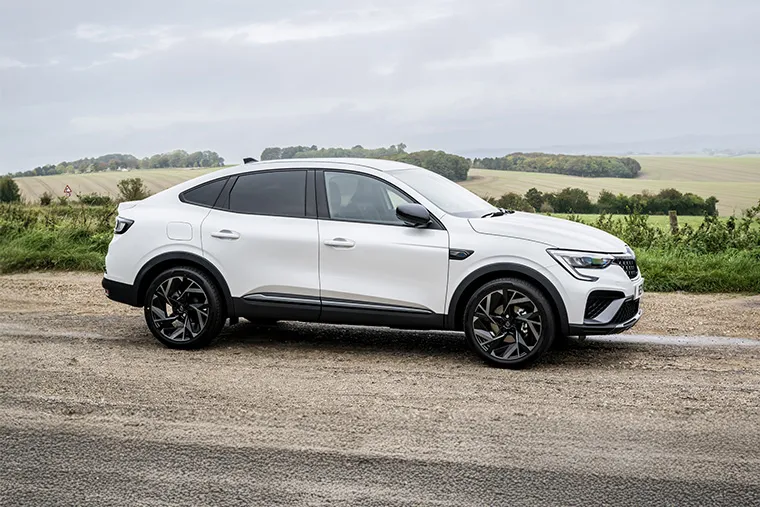 White Renault Arkana E-Tech hybrid SUV coupe parked on rural road with countryside background.