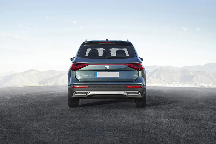 Rear view of a metallic blue SEAT Tarraco FR SUV parked on an open road with mountain scenery.