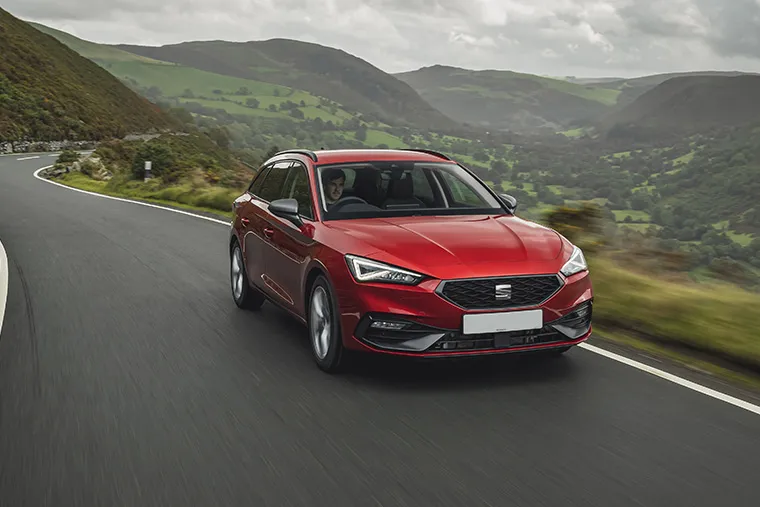 Red SEAT Leon Estate driving through scenic countryside with dramatic cloudy skies overhead