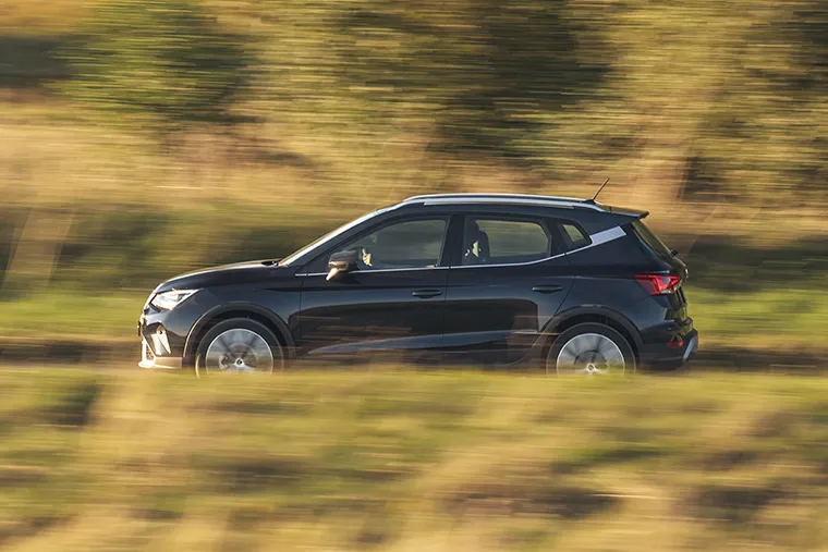 Black SEAT Arona SUV driving through the countryside on a sunny day with motion blur effect.
