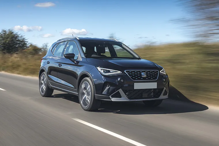 Black SEAT Arona compact SUV driving on a countryside road under a clear blue sky.