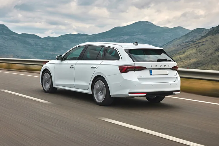 White Skoda Octavia Combi driving on a scenic highway with mountain views.