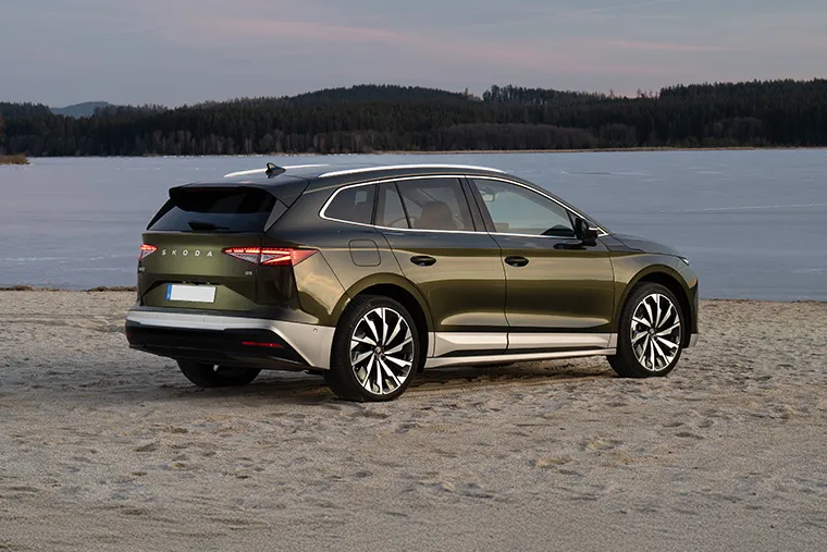 Green Skoda Enyaq iV electric SUV parked by a frozen lake at sunset.