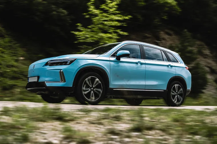 Skywell ET5 electric SUV driving through a scenic mountain road, finished in light blue with black trim and modern LED headlights