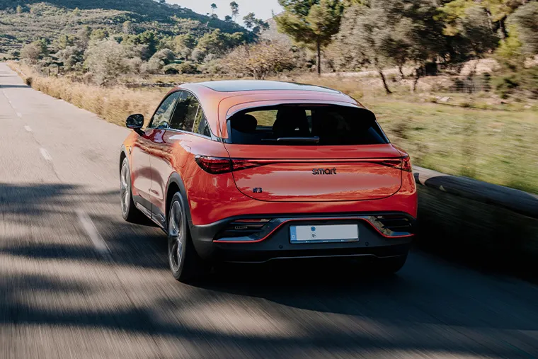 Smart #3 electric SUV driving on a scenic mountain road, finished in bright orange with a sleek coupe-style rear design