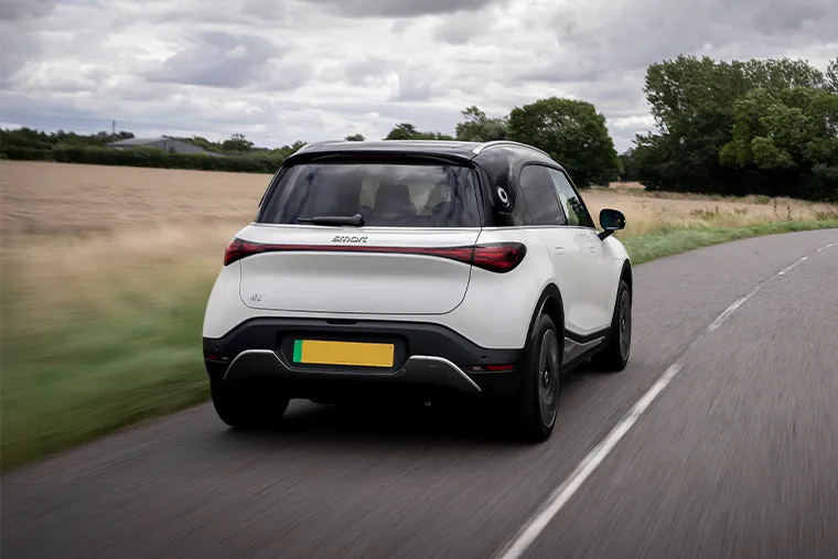 Smart #1 electric SUV driving along a country road, viewed from the rear, with cloudy skies and open fields in the background