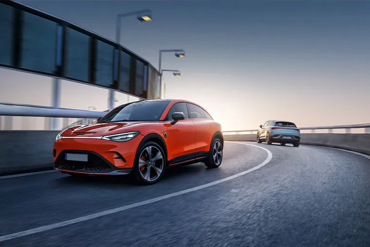 Smart #3 electric SUV driving on a curved city bridge at sunset, finished in bright orange with sporty styling