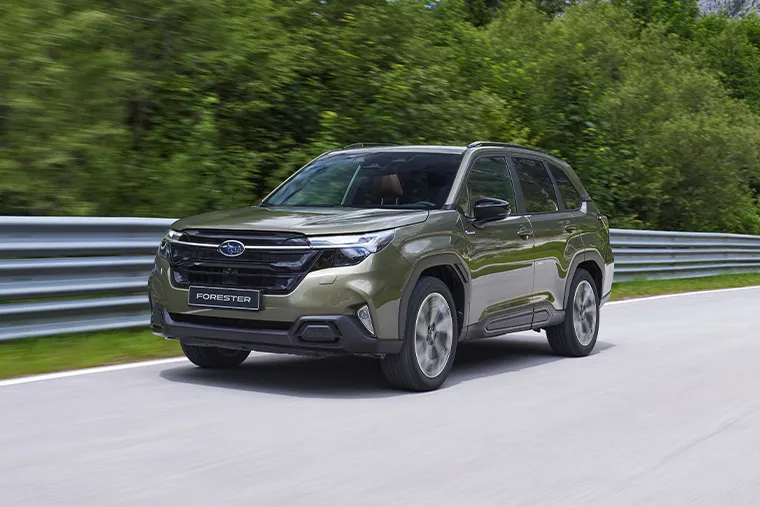Green 2025 Subaru Forester SUV driving on a road with trees in the background