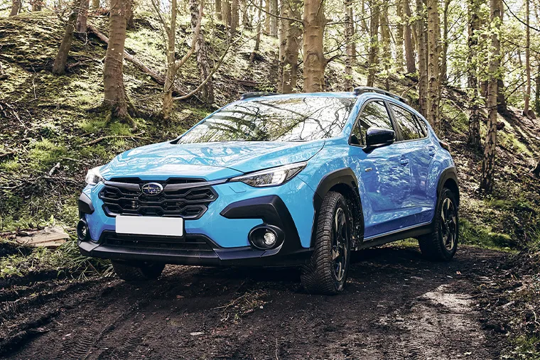 Blue 2025 Subaru Crosstrek SUV driving off-road on a muddy forest trail