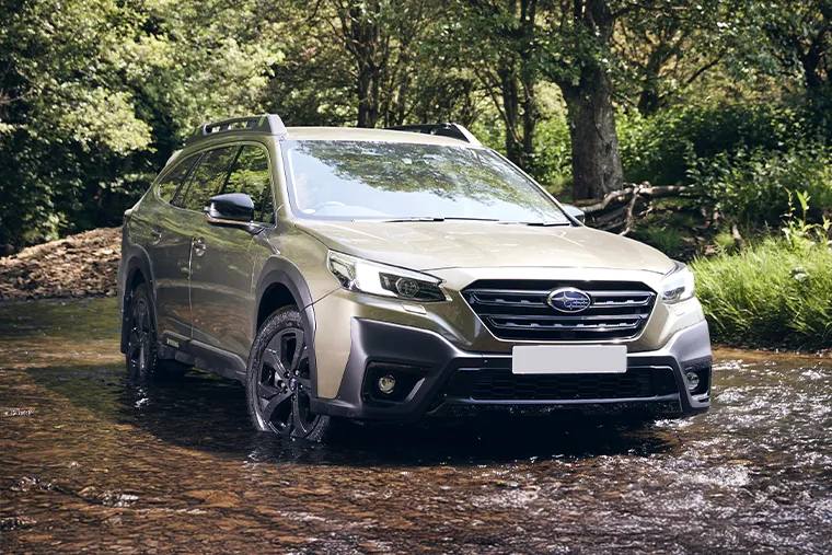 2025 Subaru Outback SUV driving through shallow water in a forest setting