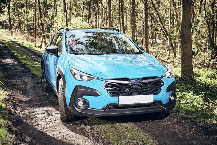 Blue 2025 Subaru Crosstrek SUV driving on a muddy forest trail