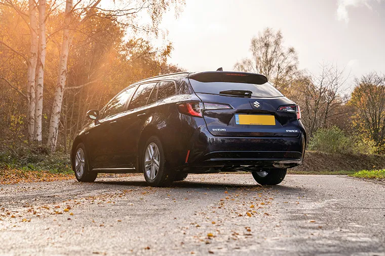 Dark Suzuki Swace estate car in autumn forest sunlight.