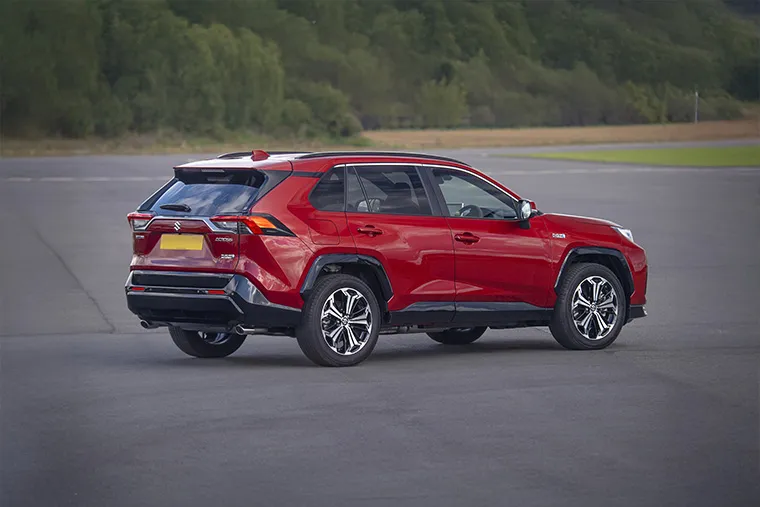 Rear-side view of red 2025 Suzuki Across Plug-in Hybrid SUV parked on tarmac.