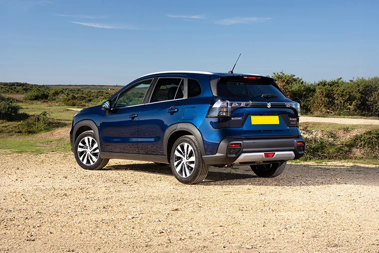 Rear and side view of blue 2025 Suzuki S-Cross Hybrid SUV parked on a dirt track.