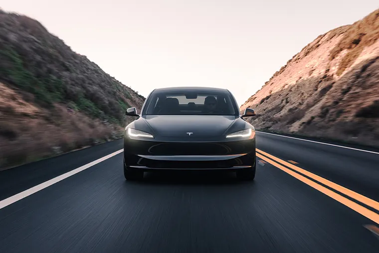 Black Tesla driving through a winding mountain road at sunset, with motion blur emphasizing speed and smoothness.