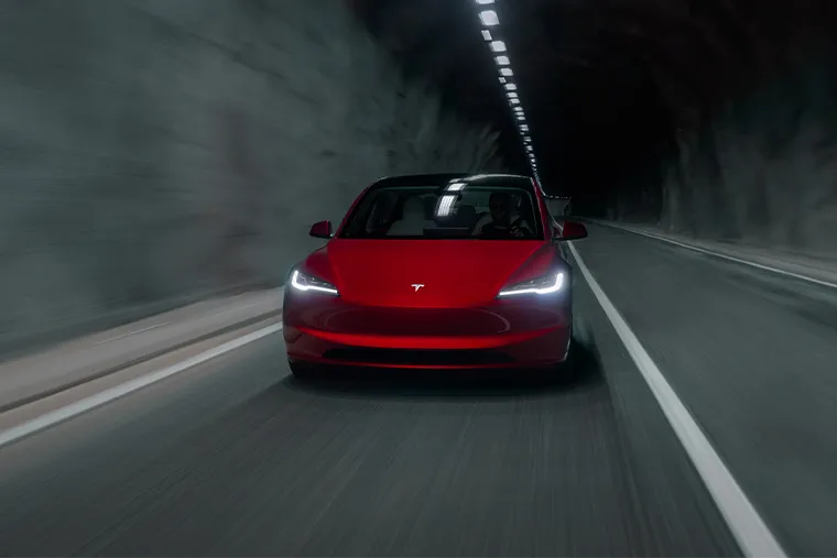 Red Tesla driving through a dimly lit tunnel with headlights on, creating a dramatic motion blur effect.