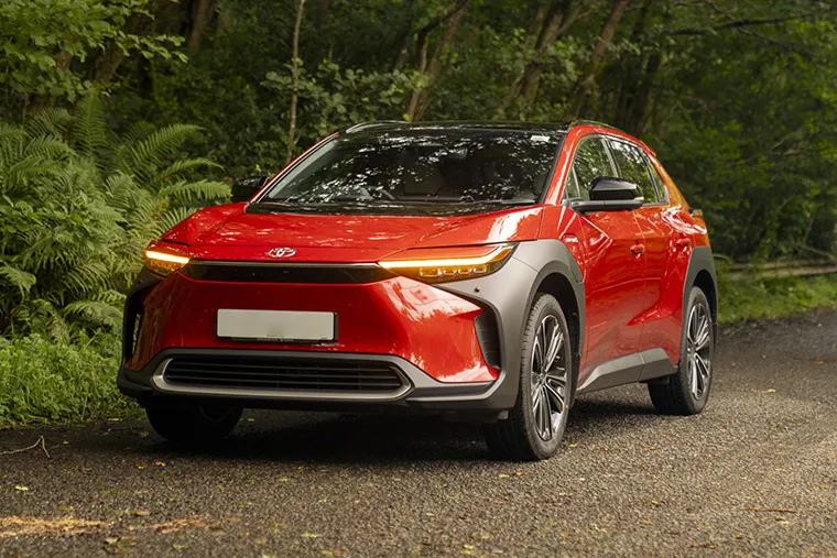Red Toyota bZ4X electric SUV parked on a forest road.