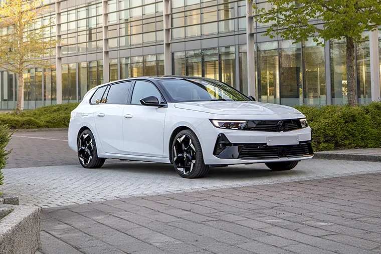 White Vauxhall Astra Sports Tourer parked in front of a modern glass office building with trees and greenery