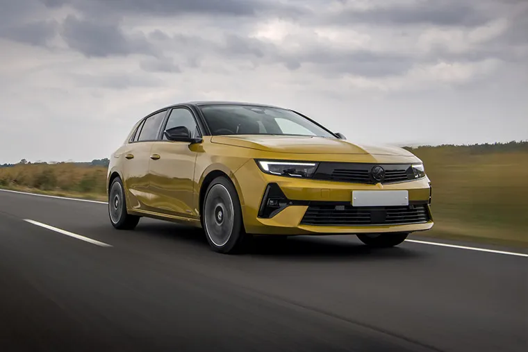 Yellow Vauxhall Astra driving on an open countryside road under a cloudy sky.