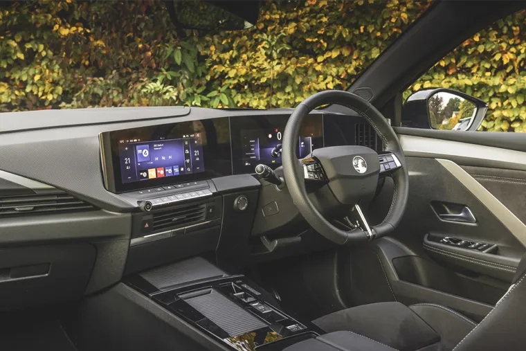 Interior view of a modern Vauxhall car showing the digital dashboard, infotainment screens, and steering wheel with stitched black seats and autumn foliage outside the window