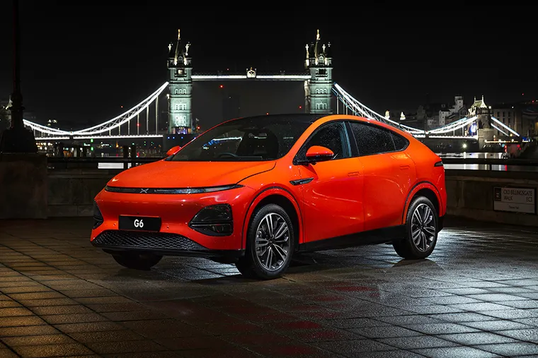 Orange XPeng G6 electric SUV coupe parked at night near London’s Tower Bridge with illuminated skyline in the background