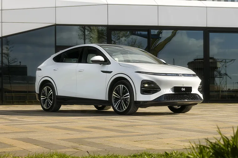 White XPeng G6 electric SUV coupe parked outside modern glass building, highlighting sleek profile and aerodynamic styling