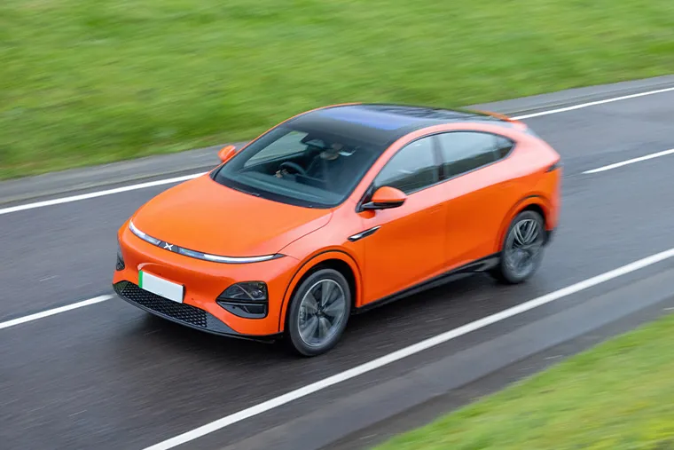 Orange XPeng G6 electric SUV coupe driving on a wet road with black roof and modern styling
